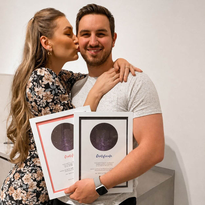 Couple kissing, holding their two framed Name a Star certificates